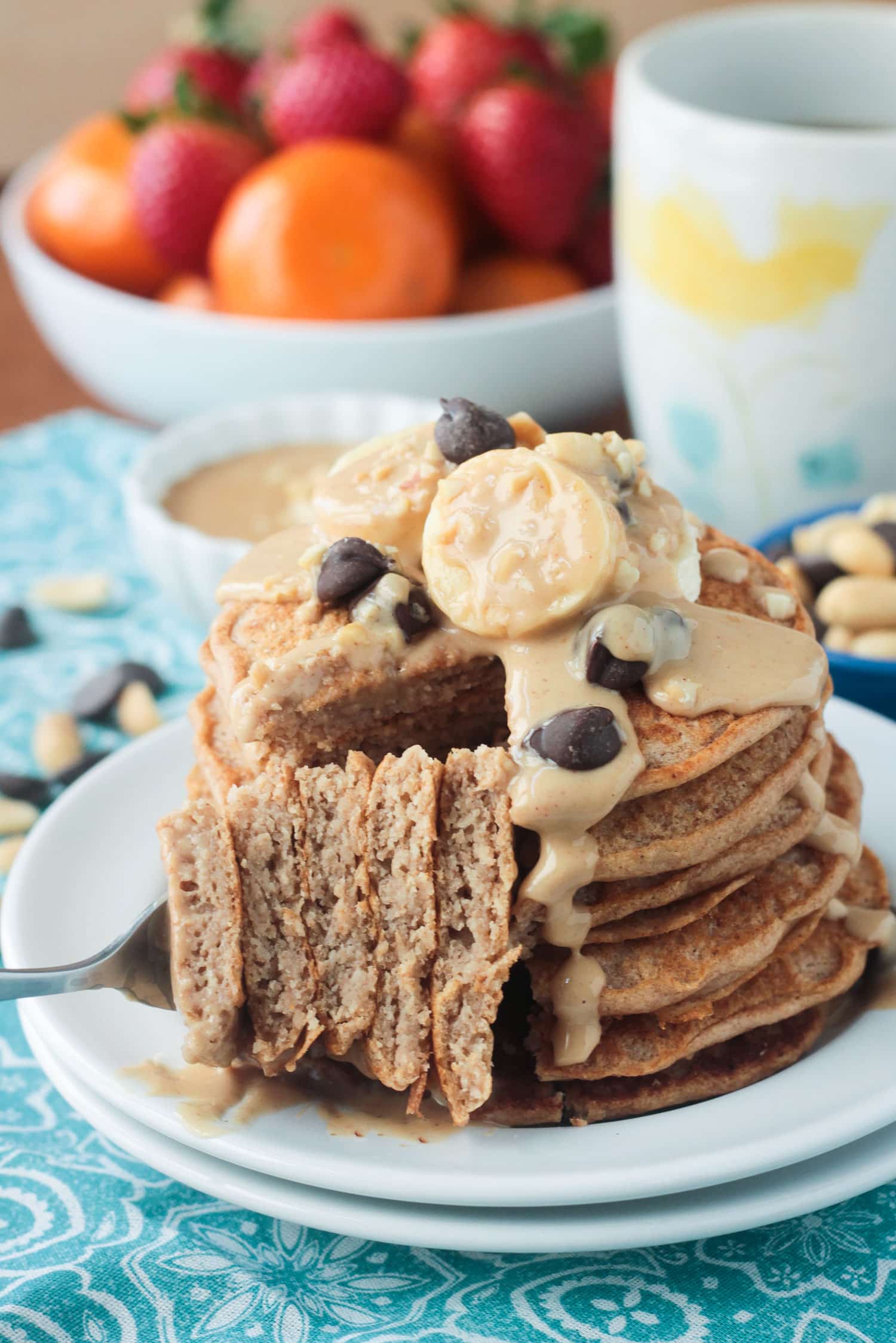 Forkful of a big bite of pancakes taken from a stack. Fresh fruit in the background.