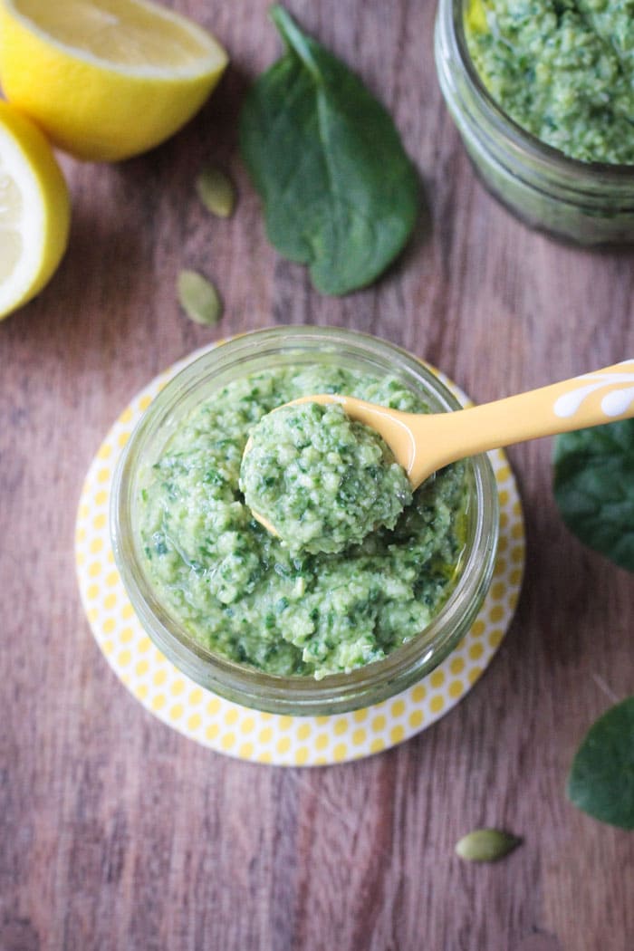 Small yellow measuring spoon scooping out a teaspoon of Spinach Artichoke Pesto from a jar.