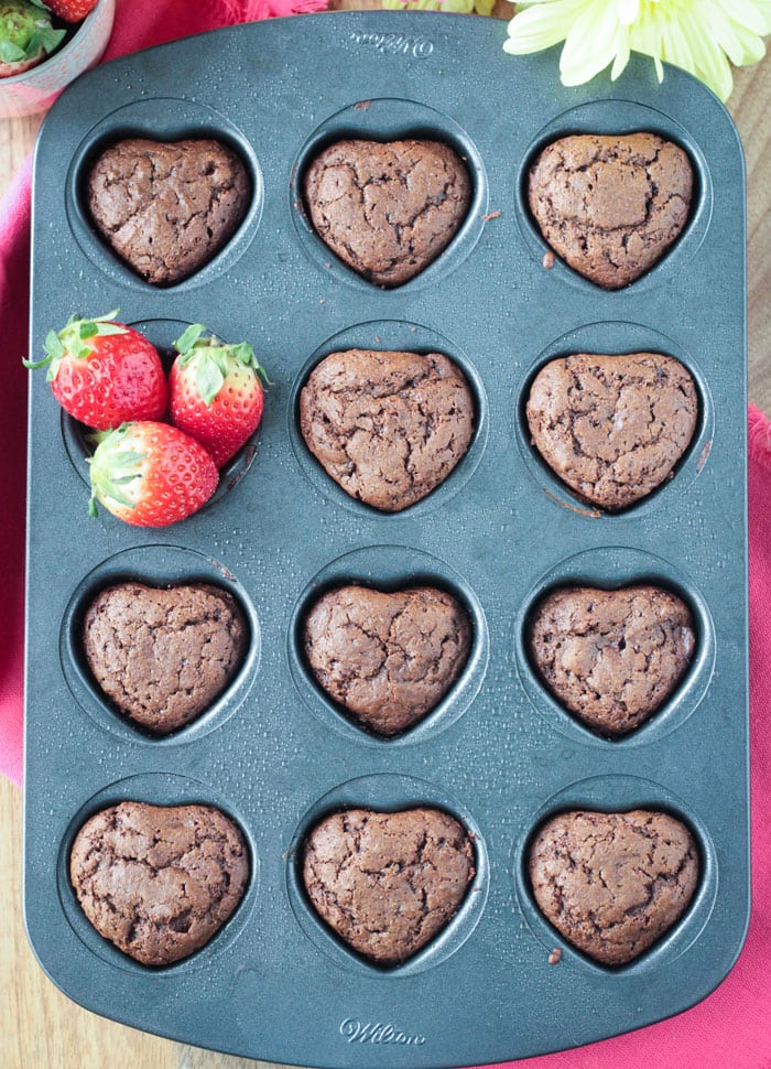 Heart shaped cupcake pan filled with chocolate cupcakes. One cavity has fresh strawberries in it instead of a cupcake.