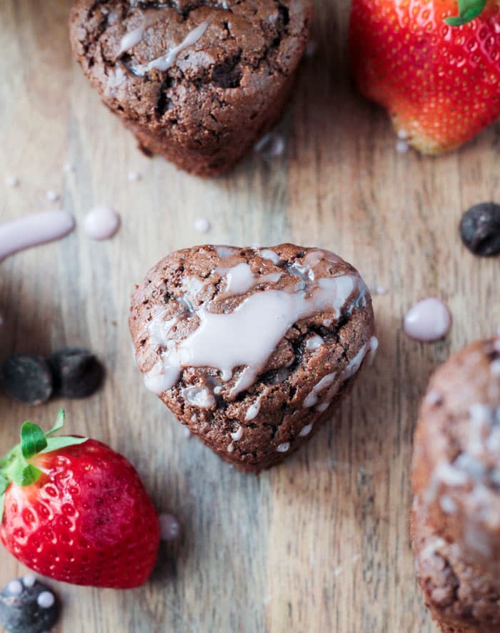 Overhead view of a Tahini Chocolate Chip Cupcake drizzled in pink icing. Fresh strawberries and chocolate chips nearby.