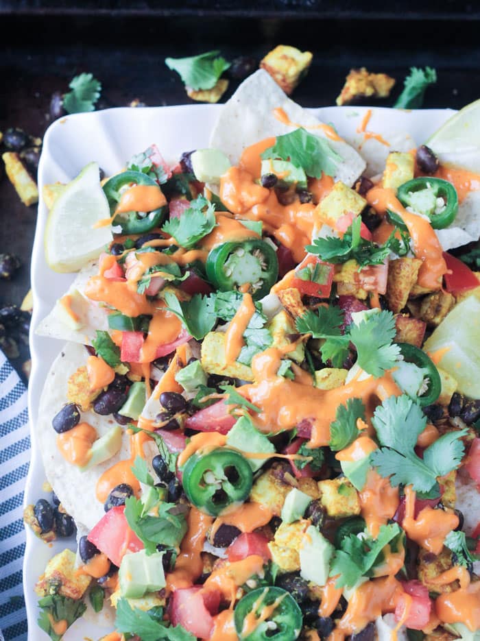 Loaded breakfast nachos on a white plate. Ingredients scattered about around the plate as well.
