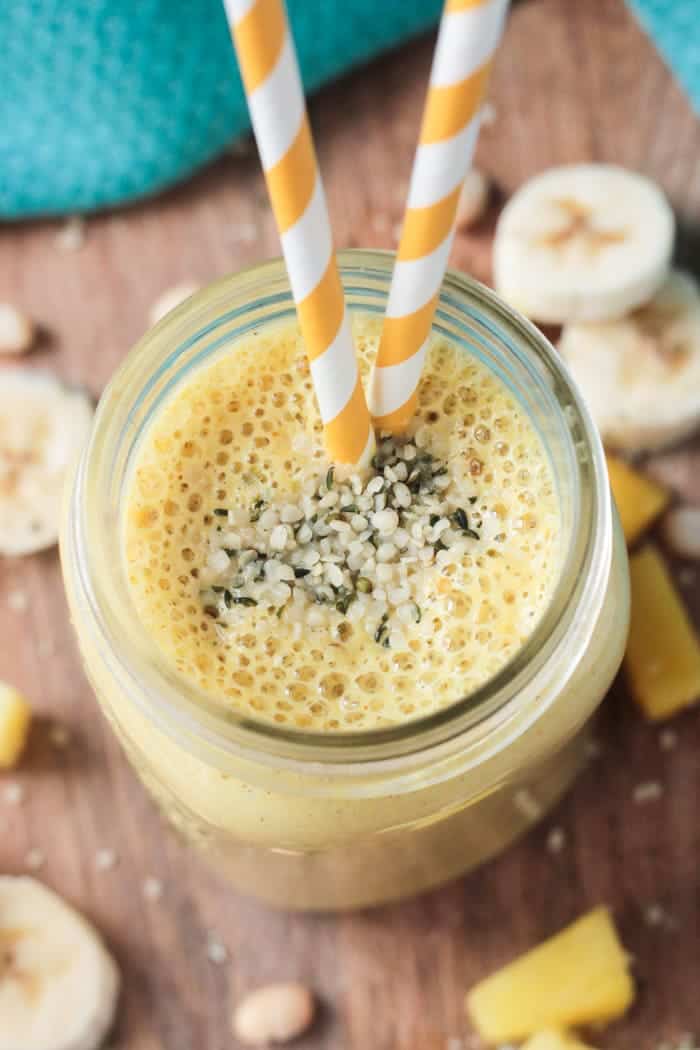 Golden yellow Pineapple Smoothie w/ orange and white straws. Banana slices on the side.