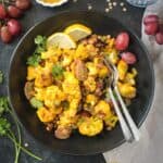 Two fork in a bowl of curry roasted cauliflower salad with lentils and grapes.