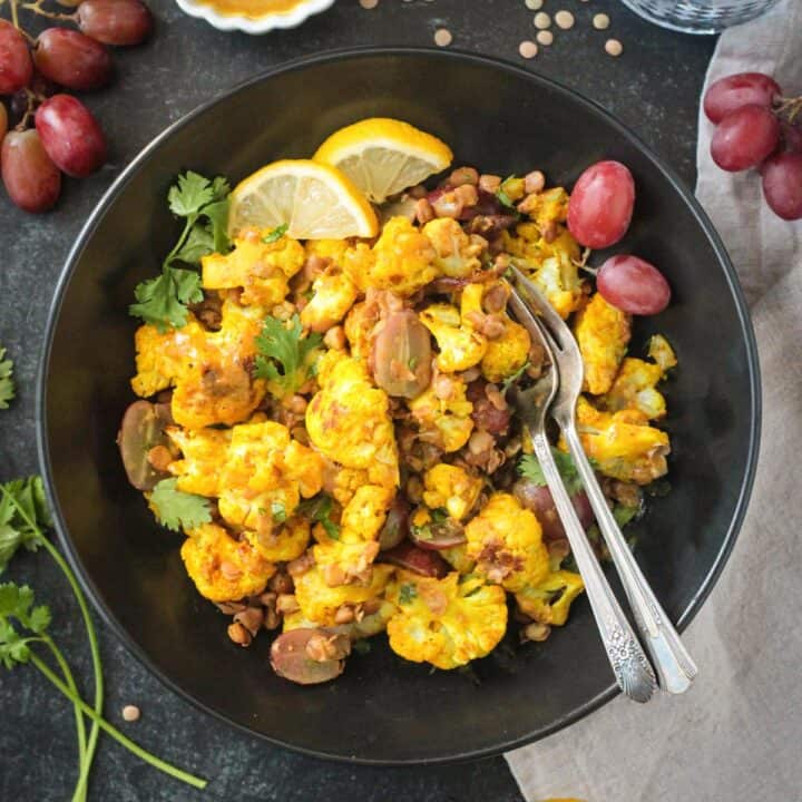 Two fork in a bowl of curry roasted cauliflower salad with lentils and grapes.
