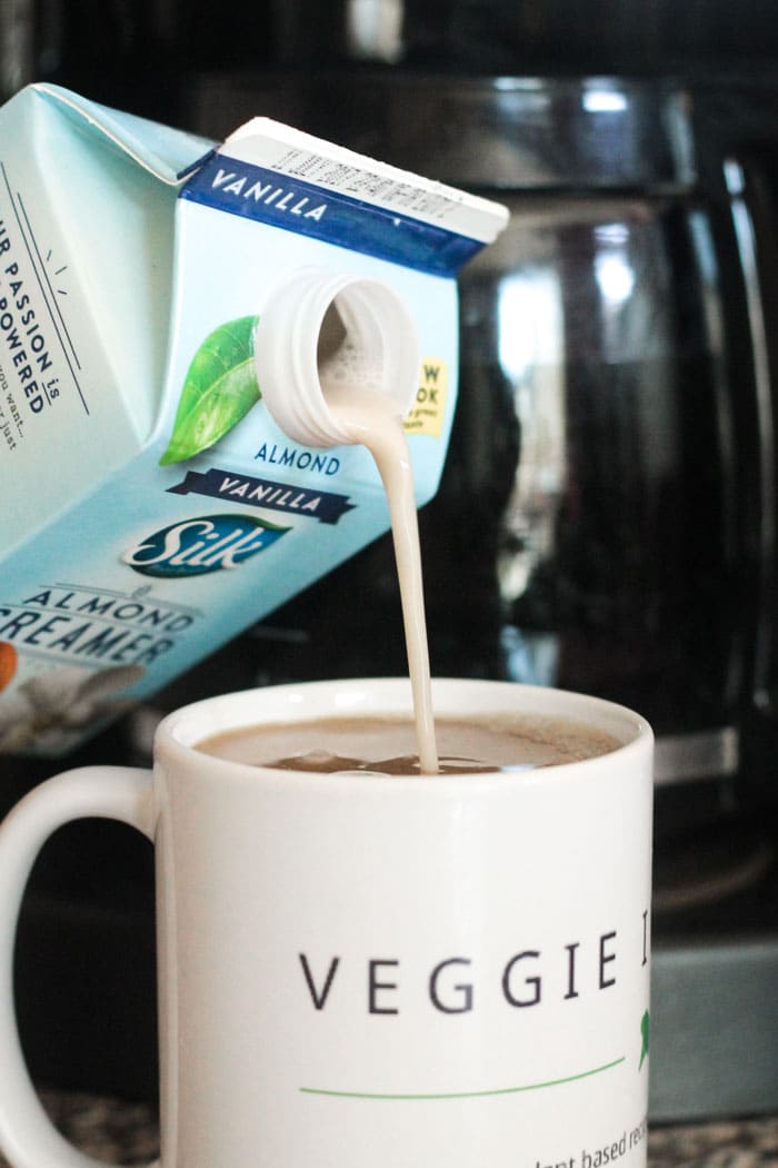 Silk Vanilla Almond Creamer being poured into a cup of coffee. Coffee pot in the background.