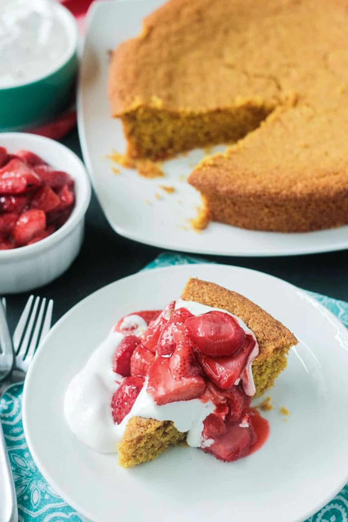 Slice of cake on a white plate with the rest of the cake behind.