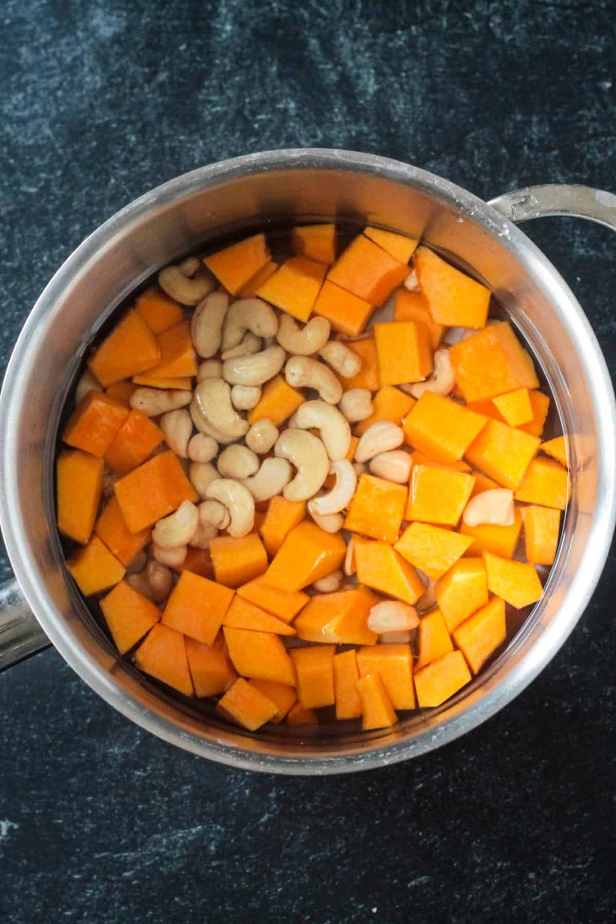 Cubed butternut squash and cashews in a pot with water.