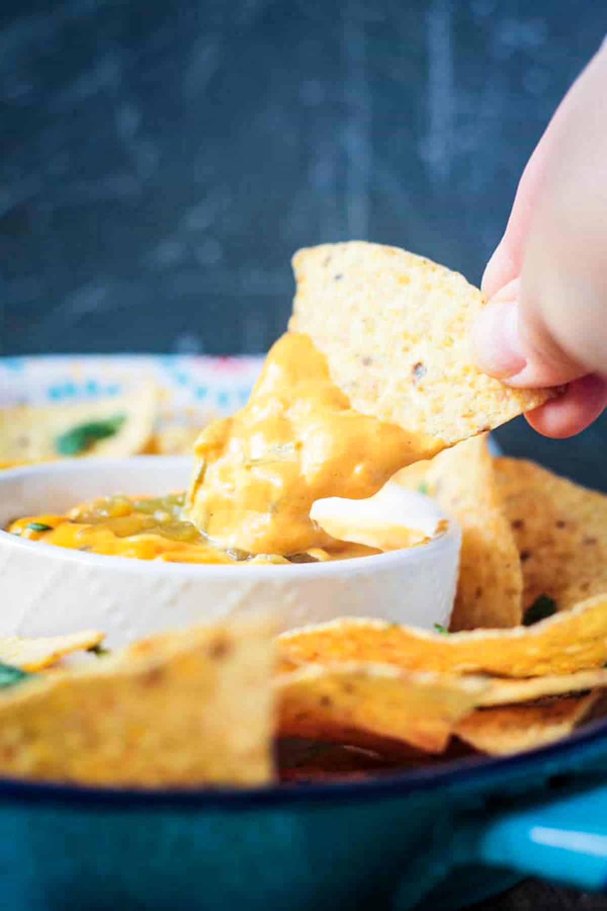 Tortilla chip dipped in a bowl of vegan nacho dip.