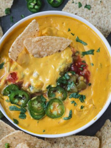 Two chips in a bowl of cashew queso topped with sliced jalapeños, cilantro, and salsa.