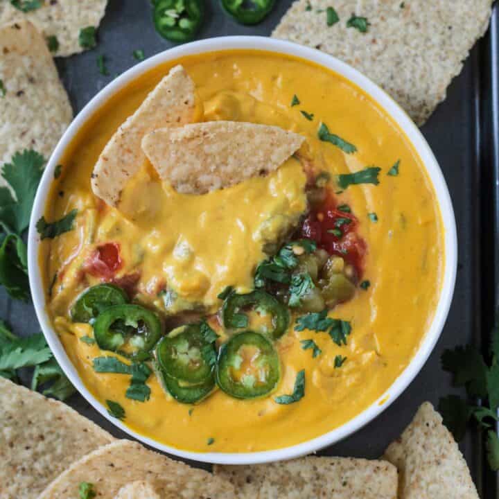 Two chips in a bowl of cashew queso topped with sliced jalapeños, cilantro, and salsa.