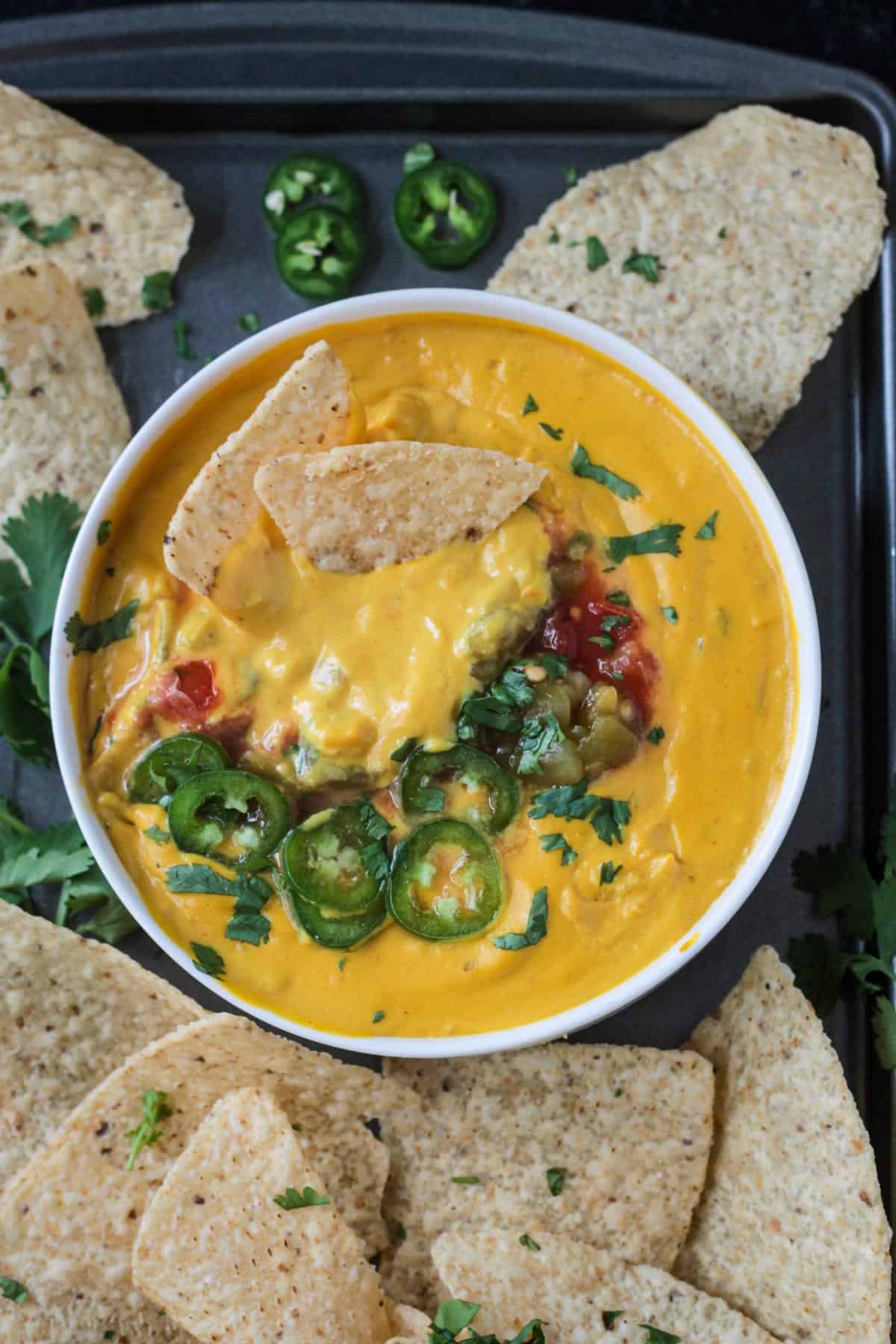 Two chips in a bowl of cashew queso topped with sliced jalapeños, cilantro, and salsa.