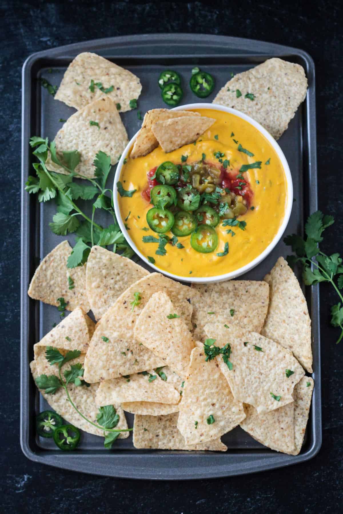 Bowl of cashew queso on a tray surrouned by tortillas chips.