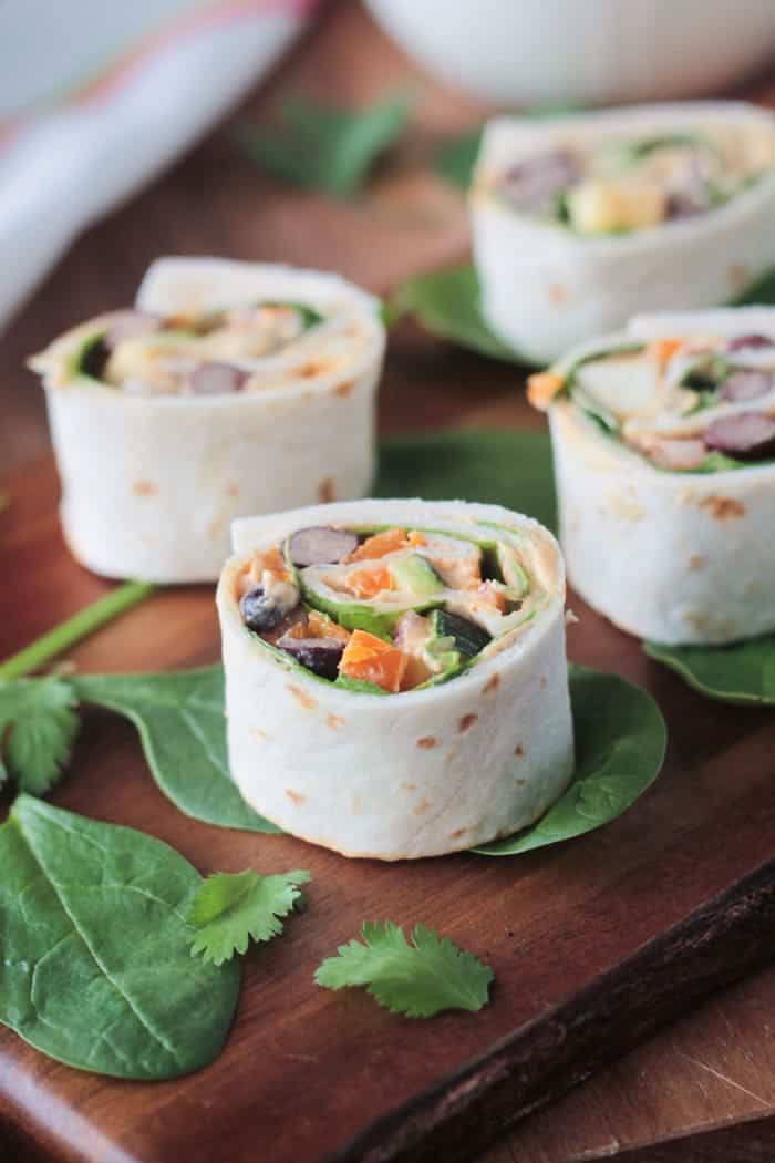 Close up of a tortilla pinwheel on top of a spinach leaf on a wooden board