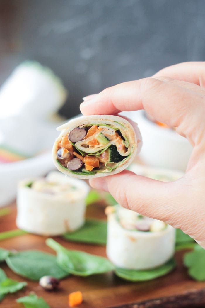 Hand holding one bite size tortilla rollup with beans and veggies