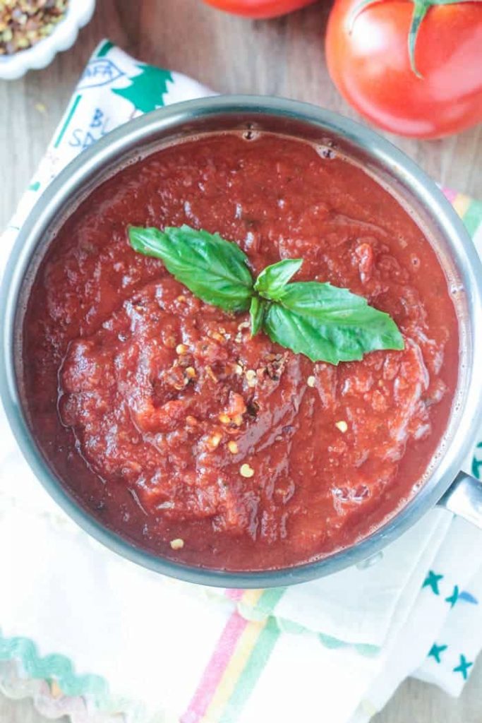 Overhead shot of Spicy Marinara Sauce in a pot with fresh basil leaves on top.