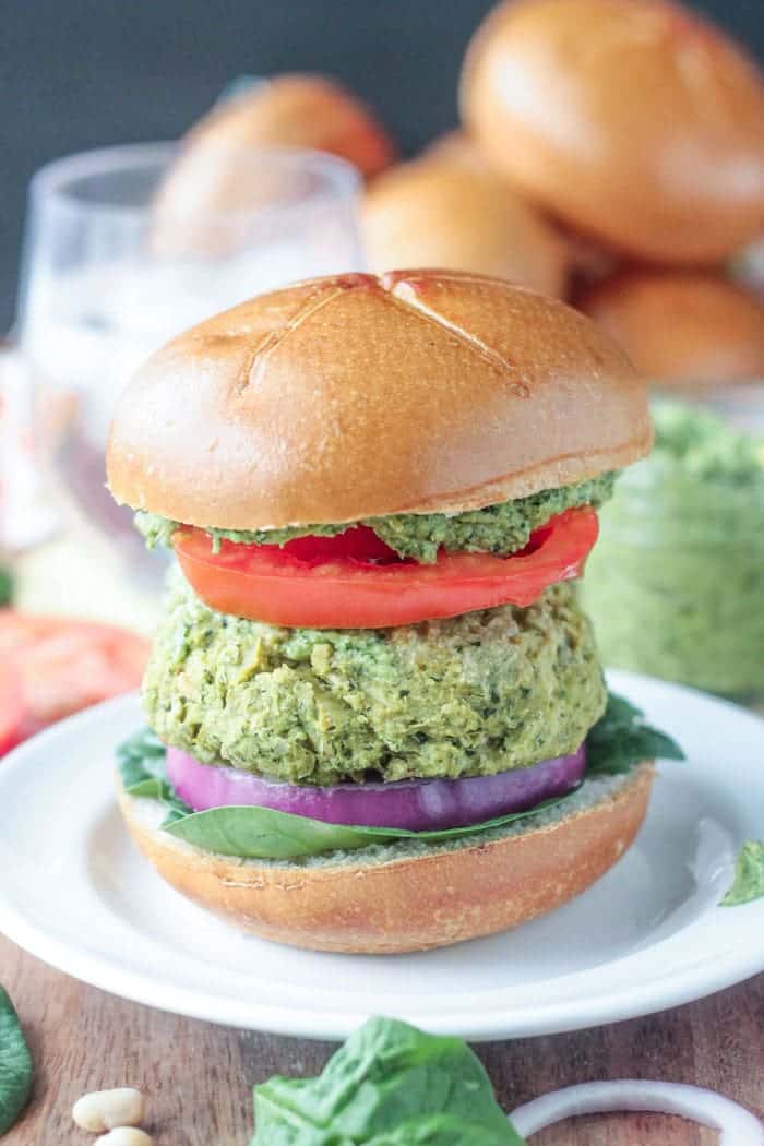 Spinach Artichoke White Bean Burgers with fresh spinach, red onion, tomato, and pesto on a wheat bun.