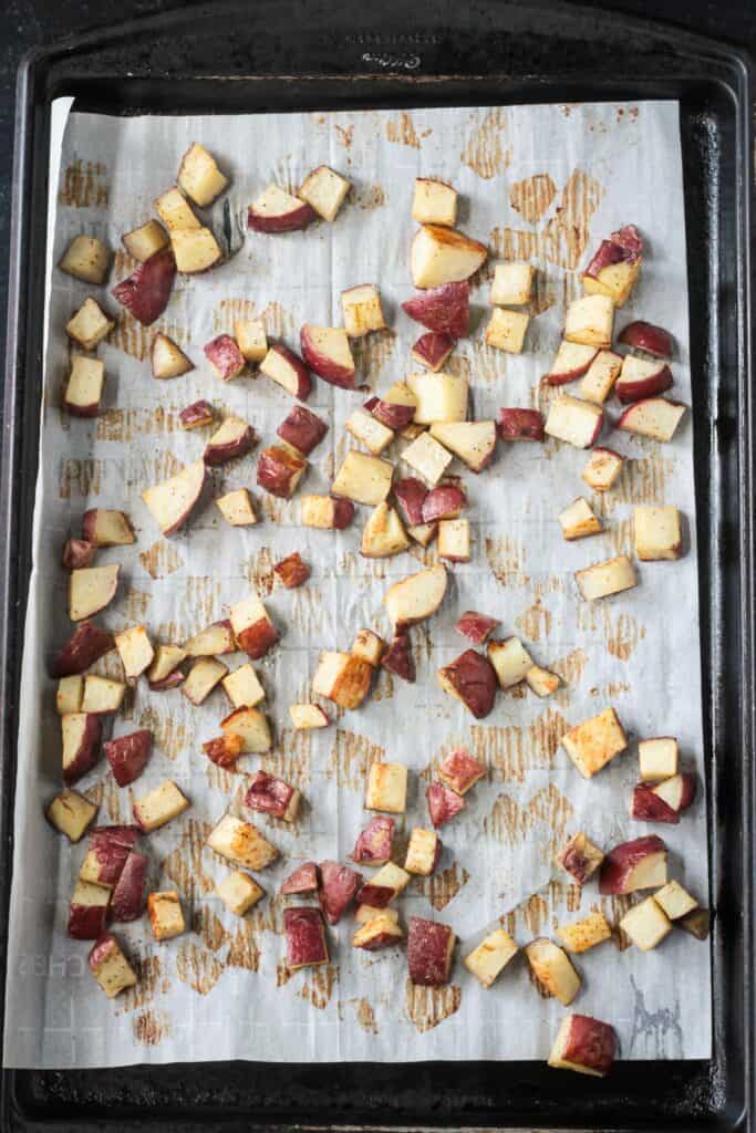 Roasted diced potatoes on a parchment lined baking sheet.