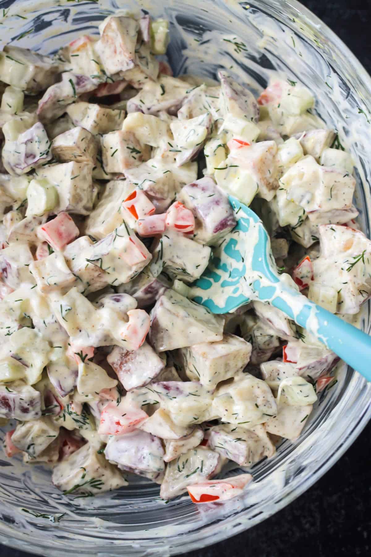 Close up of diced potatoes, celery, red peppers, and pickles mixed with creamy vegan mayo.