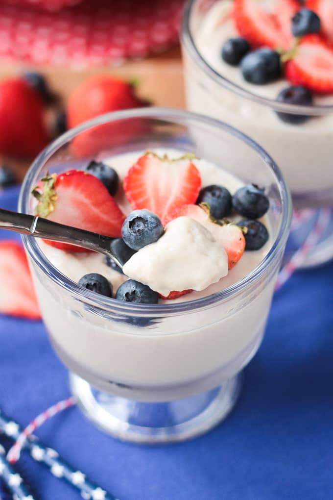 Spoon scooping vanilla vegan pudding out of a dessert glass with pudding and berries.