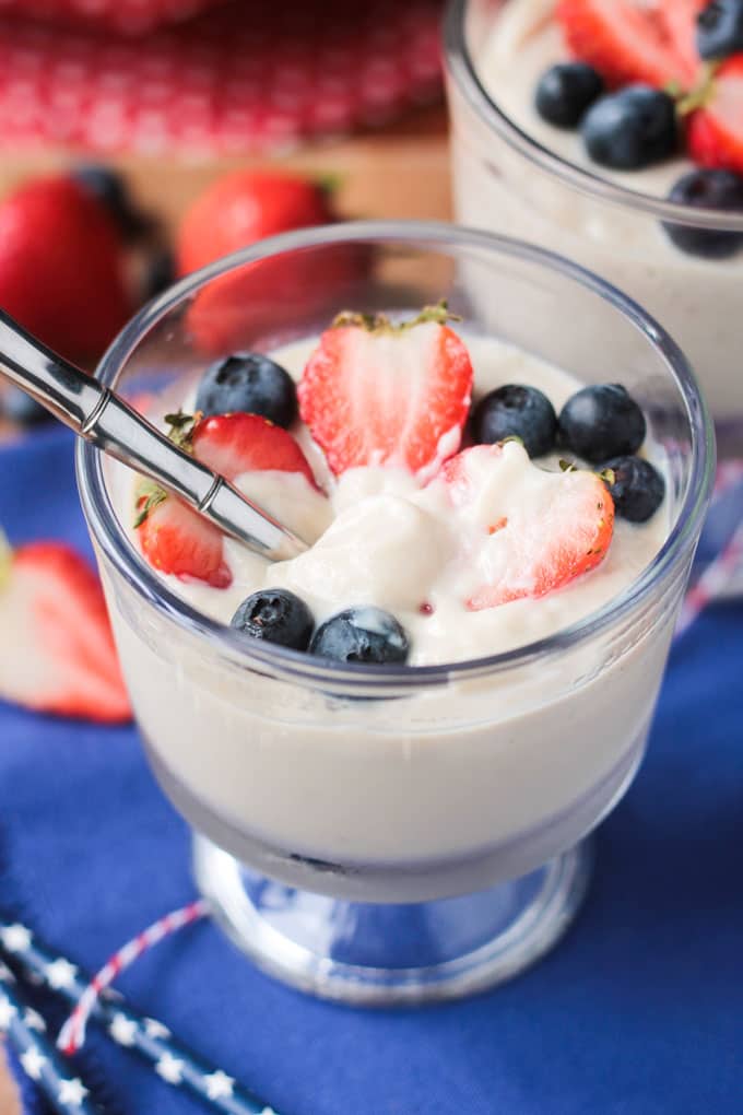 Metal spoon in a glass with vanilla vegan pudding and berries.