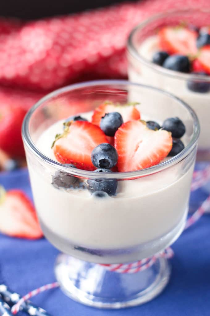 Dessert glass of vanilla vegan pudding topped with blueberries and halved strawberries. 