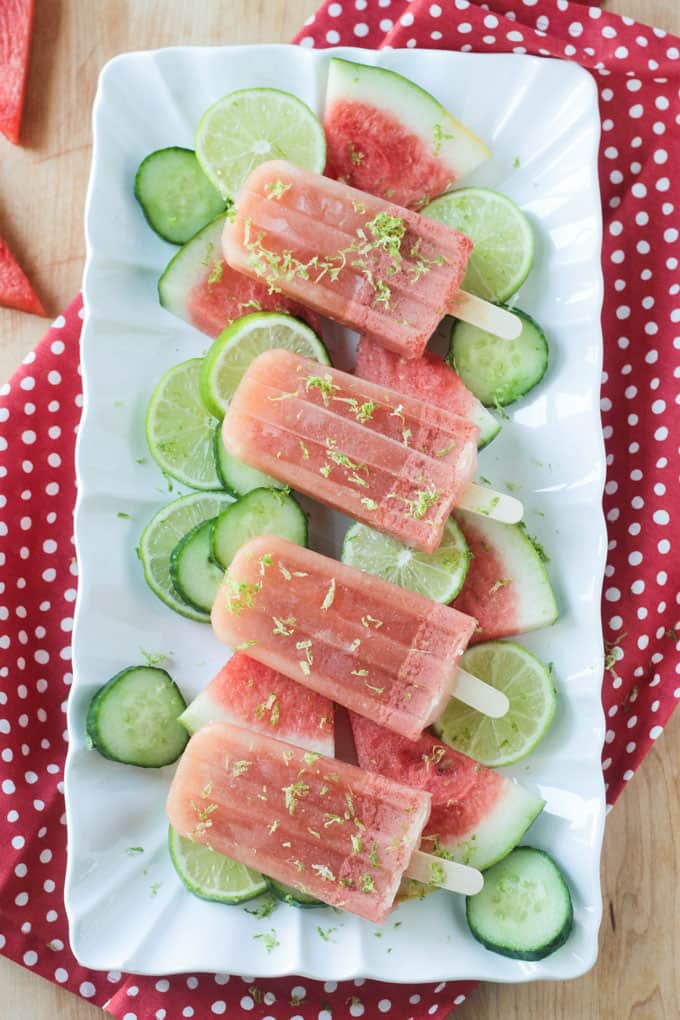 White platter holding 4 pink popsicles lying on top of fruit and vegetables slices.