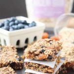 Stack of 3 Ancient Grains Breakfast Bars w/ parchment in between. Bowl of blueberries in the background.