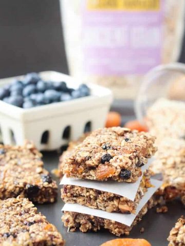 Stack of 3 Ancient Grains Breakfast Bars w/ parchment in between. Bowl of blueberries in the background.