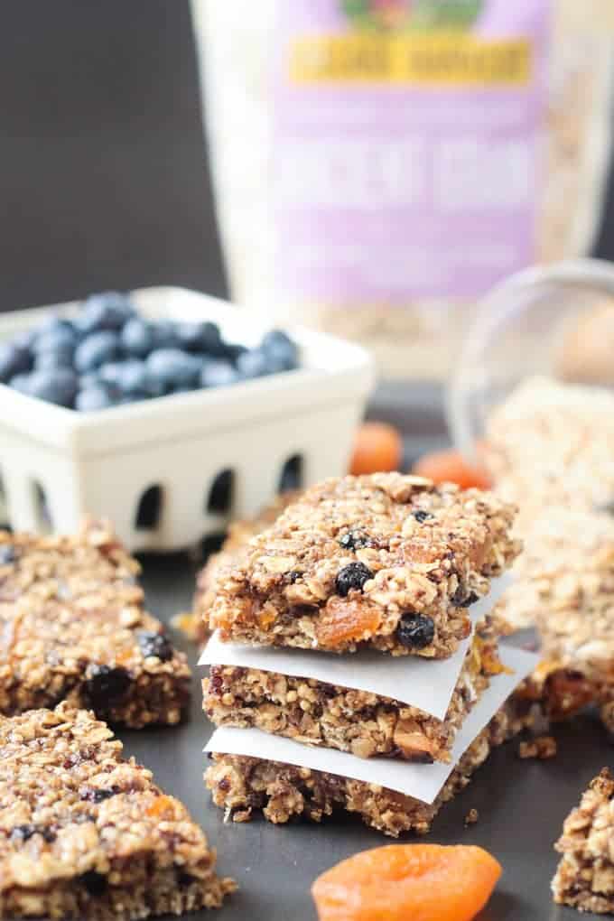 Ancient Grains Breakfast Bars - made with Organic Ancient Grains along with seeds and dried fruit for a nutritious hearty breakfast or snack. Lunchbox friendly too! Stack of 3 Ancient Grains Breakfast Bars w/ parchment in between. Bowl of blueberries in the background.