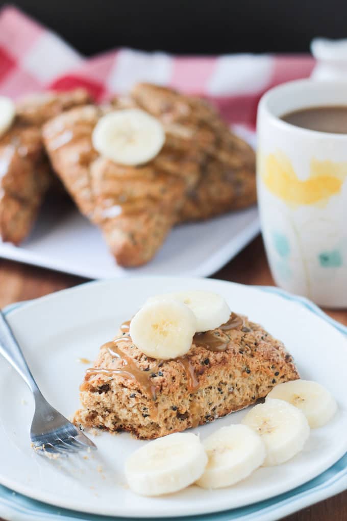 Bite taken out of a banana scone on a white plate topped with two slices of fresh banana. 