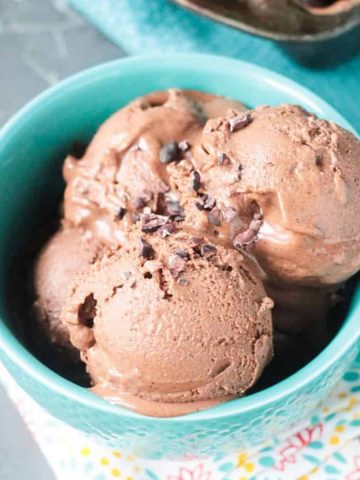 3 scoops of homemade chocolate ice cream in a blue bowl topped with cacao nibs.