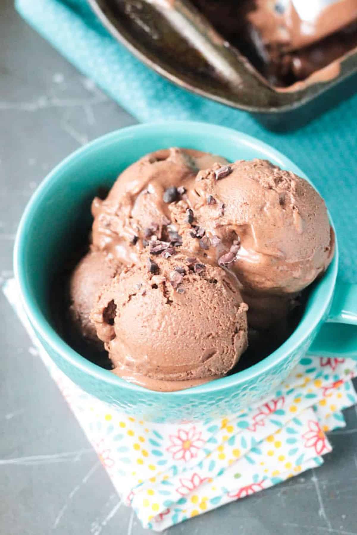 3 scoops of homemade chocolate ice cream in a blue bowl topped with cacao nibs