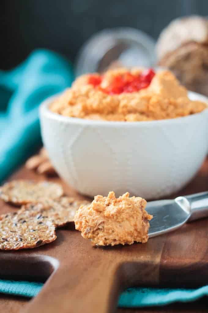 Metal cheese spreader with vegan cheddar cheese spread. Bowl of cheese spread in the background.