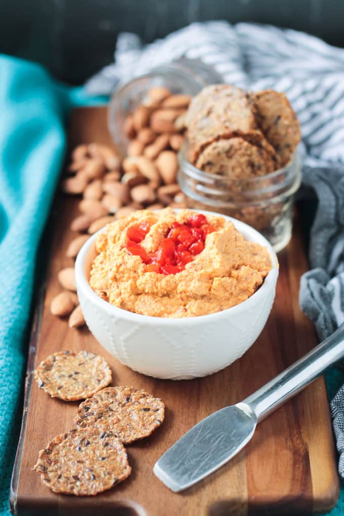 Bowl of vegan cheddar cheese spread surrounded by crackers and raw almonds.