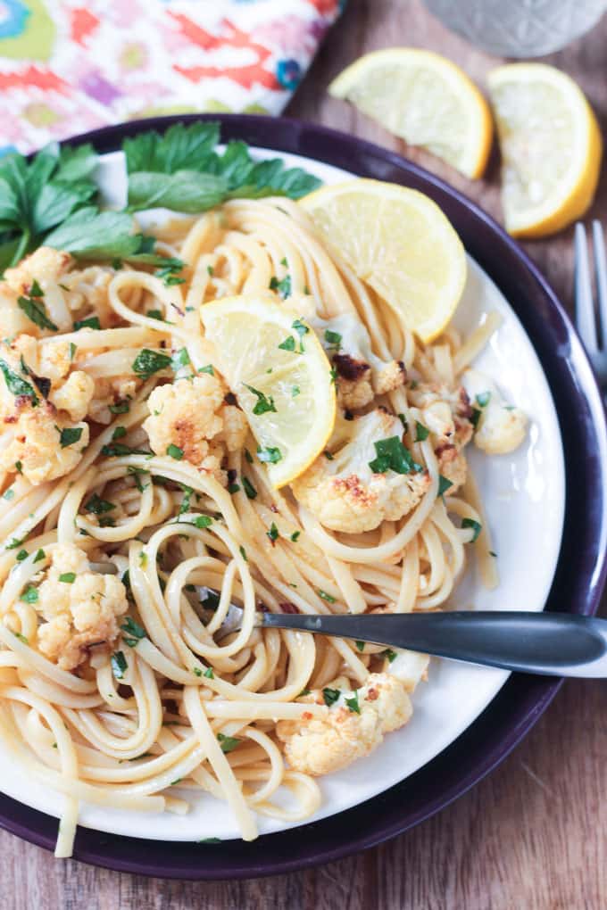 Fork swirling noodles on a plate of linguine with cauliflower and lemon wedges.