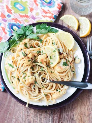 Plate of Cauliflower Scampi in Lemon Garlic White Wine Sauce garnished with wedges of lemon and fresh parsley.