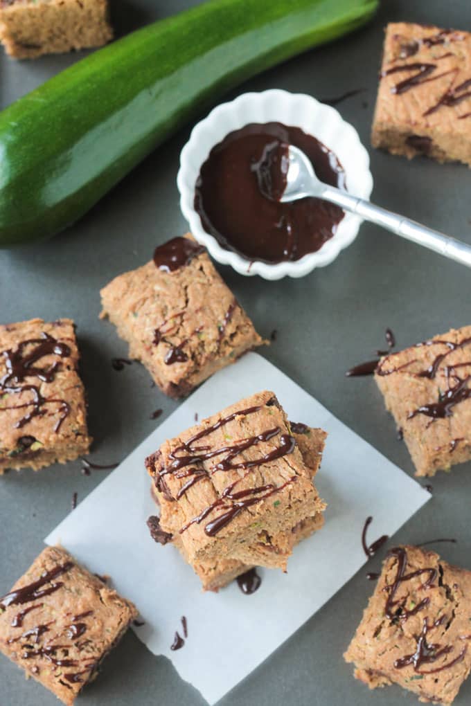 Tray of zucchini chocolate chip snack bars next to a bowl of chocolate sauce.