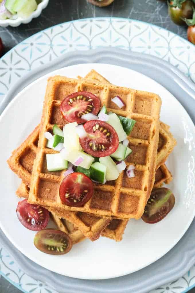 Crunchy Corn Waffles from Bold Flavored Vegan Cooking by Celine Steen. These savory waffles have hints of citrus and just enough spice to keep things interesting. The flavors are perfectly balanced. Pair them with traditional breakfast fare or serve them up alongside chili, soup, hot pepper jelly, or fresh garden salsa. You'll be addicted to these crunchy cornbread waffles like I am! Stack of crunchy corn waffles topped with diced veggies.