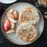 Two bagel halves spread with vegan maple walnut cream cheese on a plate with apple slices.