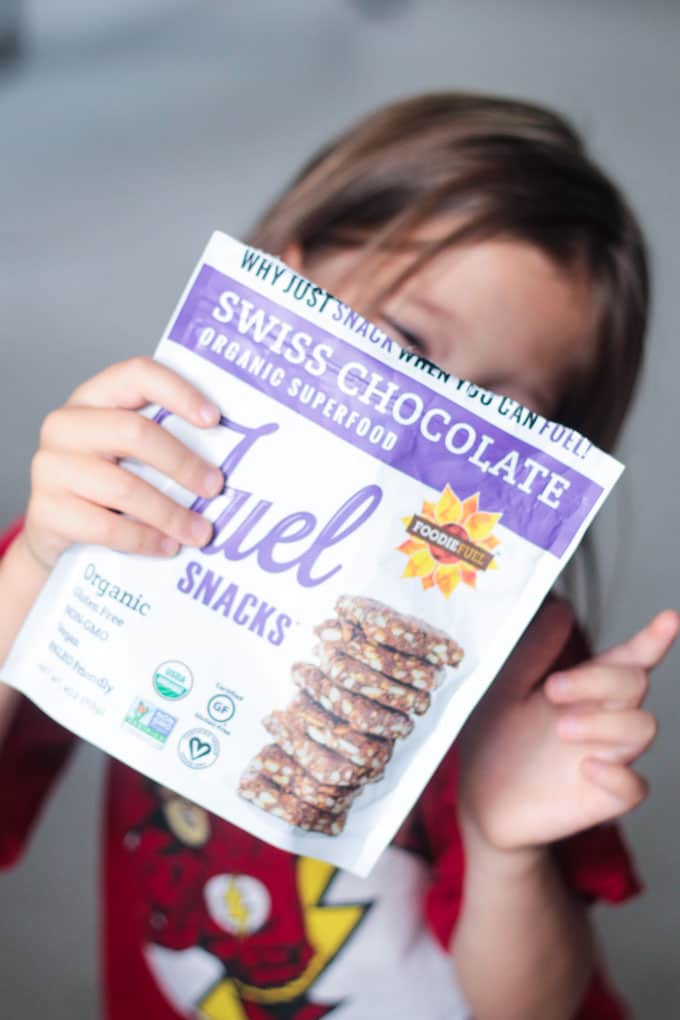 Young girl holding a package of Foodie Fuel Swiss Chocolate Crackers in front of her face.