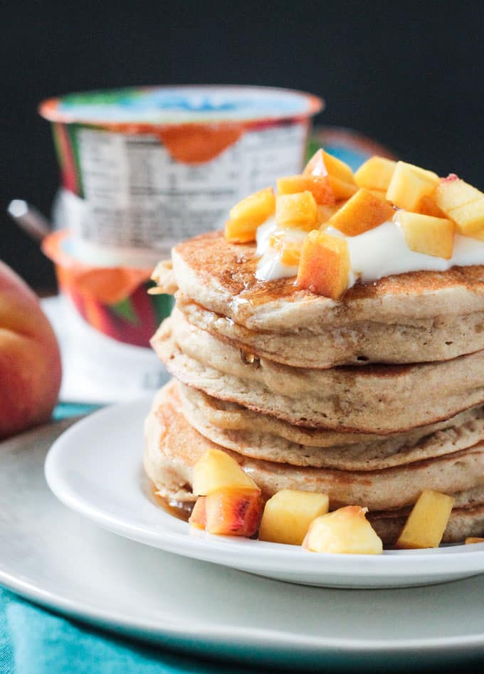 Tall stack of pancakes topped with Silk dairy free yogurt and fresh peaches.