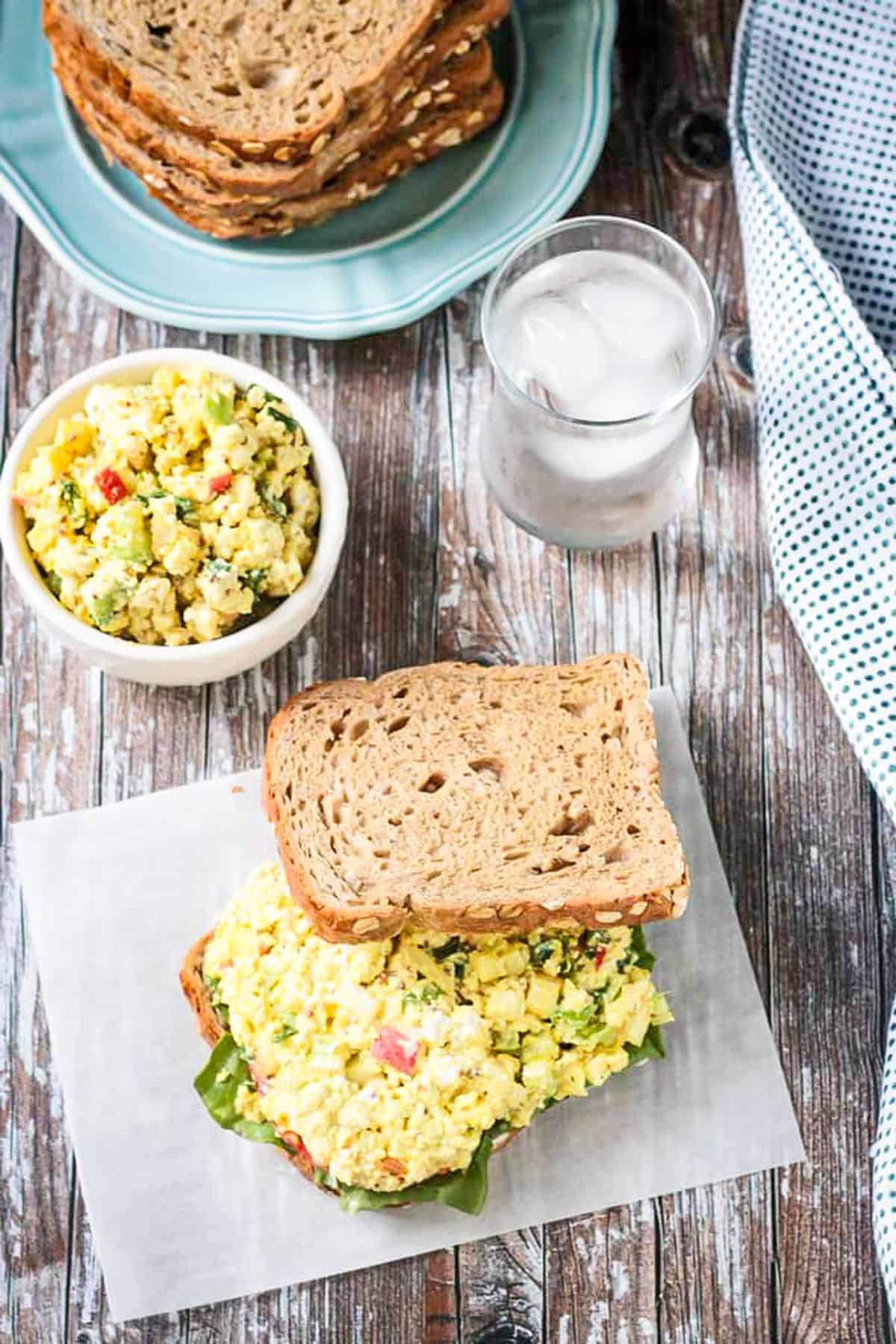 Vegan egg salad on whole grain bread with glass of water behind.