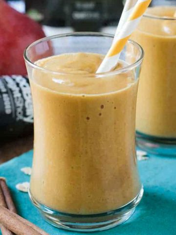 Pumpkin pear smoothie in a glass with an orange and white straw.