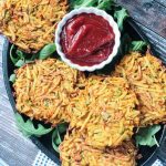 Plate of veggie potato fritters on arugula with a small bowl of spicy ketchup.