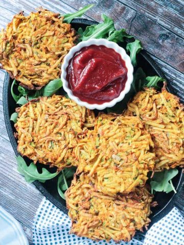 Plate of veggie potato fritters on arugula with a small bowl of spicy ketchup.