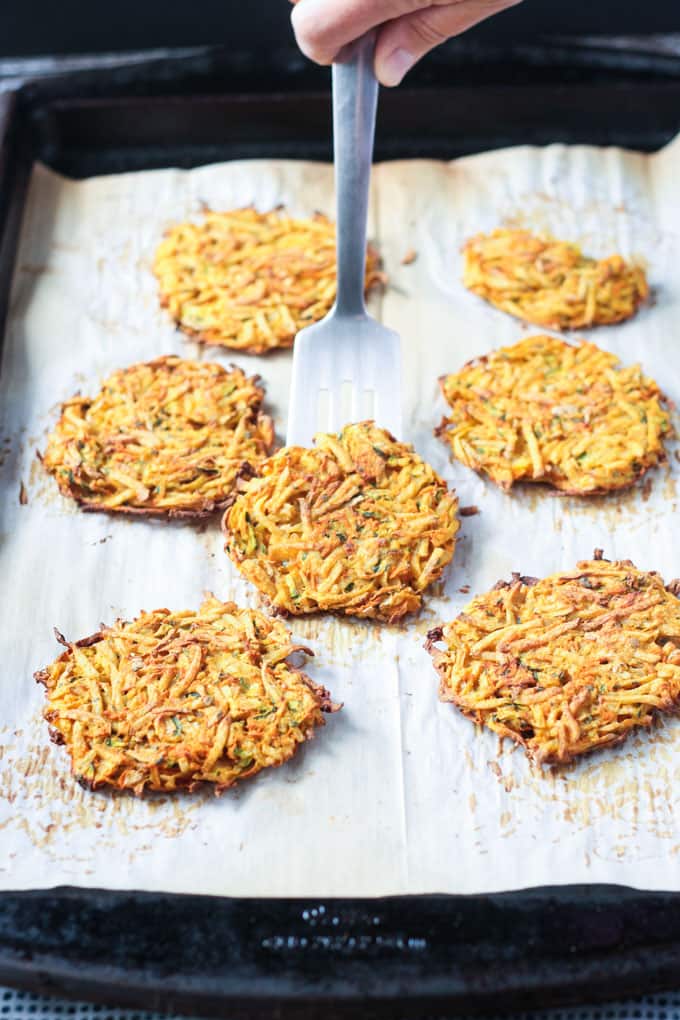 Potato fritters on parchment paper on a baking tray.