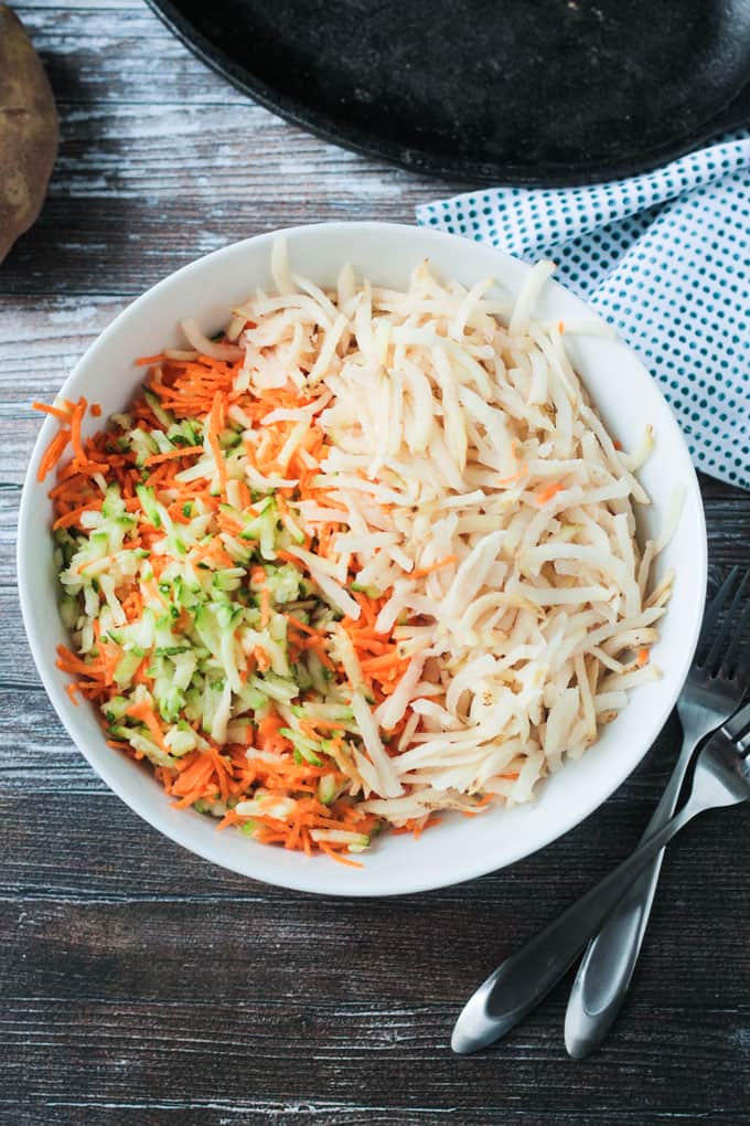 Bowl of shredded potatoes, shredded, zucchini, and shredded carrots.