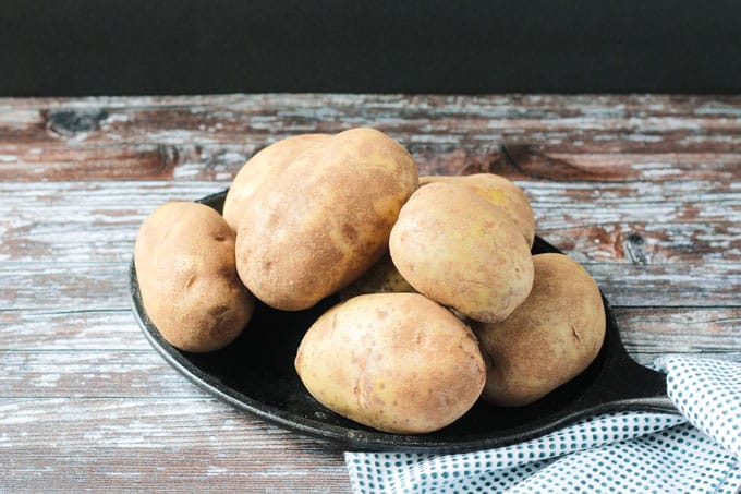 Russet potatoes stacked up a black plate on a wooden board.