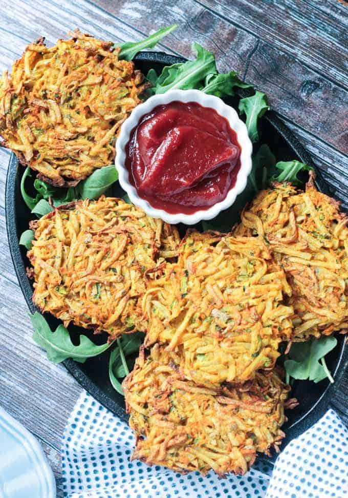 Plate of veggie potato fritters on arugula with a small bowl of spicy ketchup.