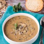Bowl of wild rice soup on a blue kitchen towel. Slices of baguette in the background.